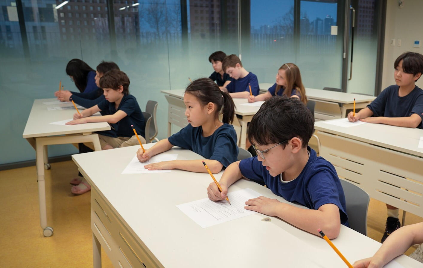 A Korean language teacher engages in a one-on-one lesson with a foreign student, using laptops and traditional Korean fan materials to support interactive learning.